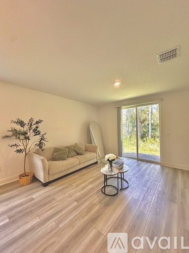 A living room with a white couch, a small table with a vase of flowers, and a plant.