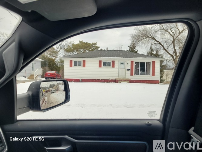 A car's side mirror reflects a red car and a white house with a black roof.