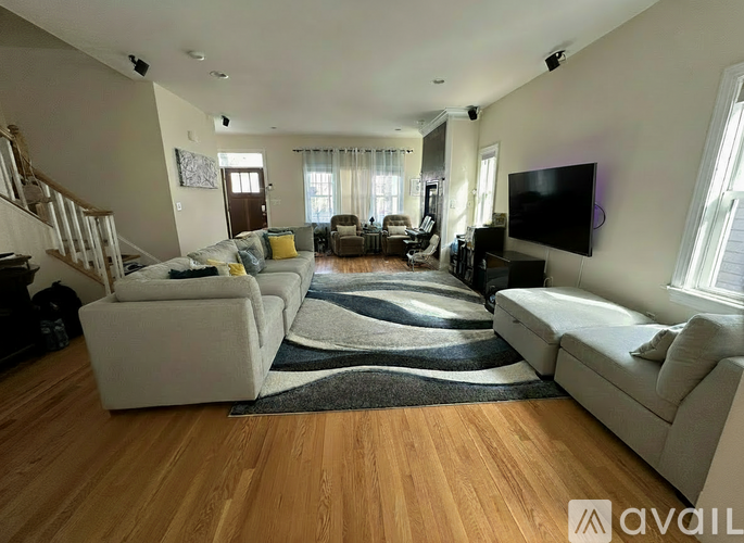 A living room with a white couch, a white chair, a white ottoman, a black and white rug, and a television mounted on the wall.