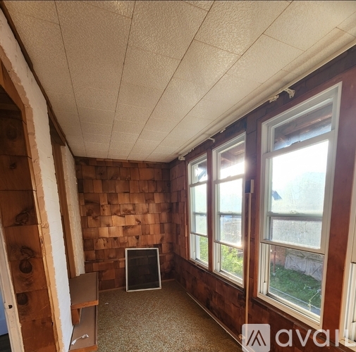 A room with wooden walls and a window showing a view of a tree and a building outside.