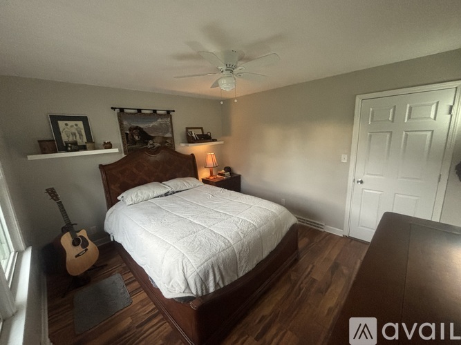A bedroom with a bed, guitar, and shelf with pictures.