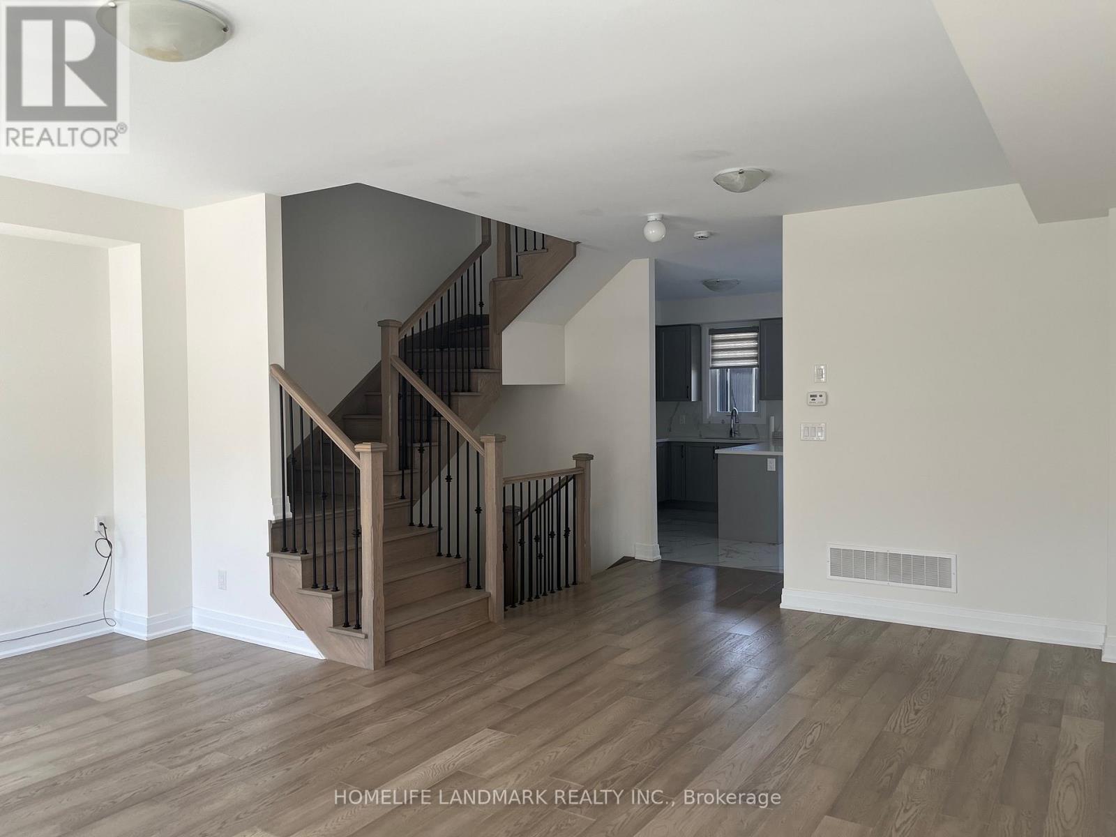 A spacious room with wooden floors and a staircase leading to another level.