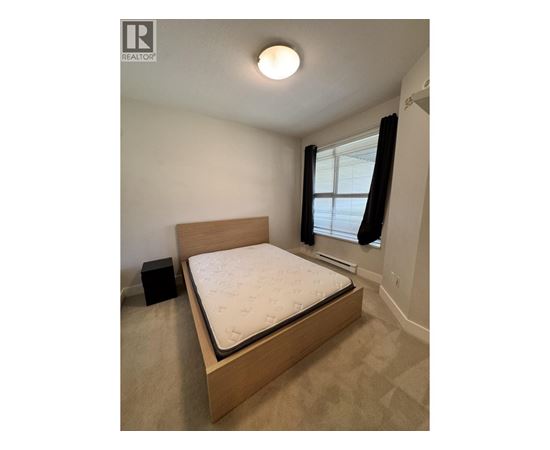 A bedroom with a bed, a window with black curtains, and a speaker on the floor.