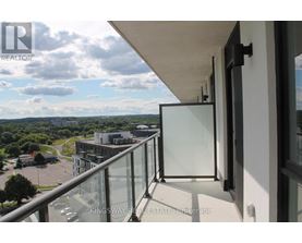 A balcony with a glass railing overlooks a parking lot and buildings.