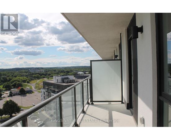 A balcony with a glass railing overlooks a parking lot and buildings.