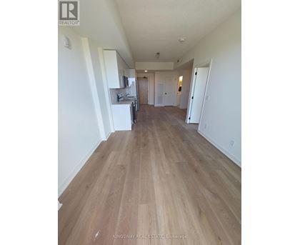 A real estate listing photo of a large empty room with wood flooring.
