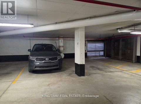 A car is parked in a garage with a white ceiling and a yellow line on the floor.