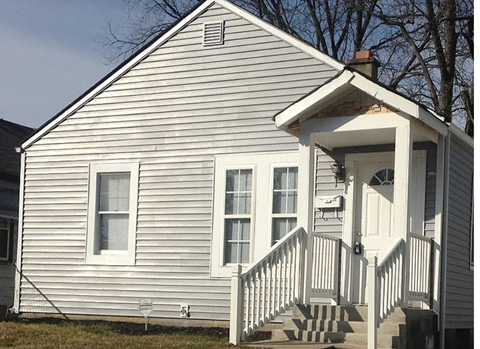 A small white house with a porch and a staircase leading to the front door.