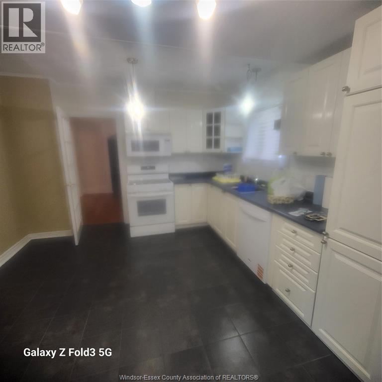 A kitchen with white cabinets and black flooring.