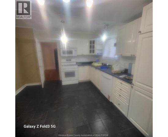 A kitchen with white cabinets and black flooring.