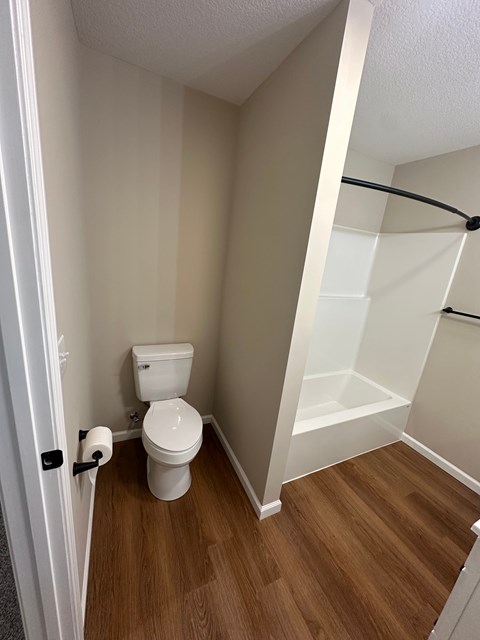 A white toilet in a small bathroom with wood flooring.