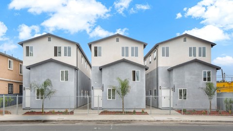Three houses with grey and brown facades are lined up on a street.
