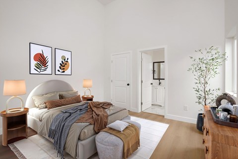 A bedroom with a bed, two lamps, a bench, and a plant.
