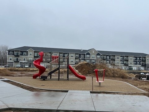 A playground with a red slide in front of a grey apartment building.