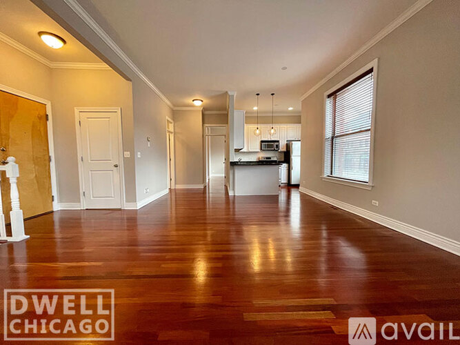 A spacious room with wooden floors and a kitchen area in the background.