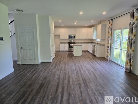 A spacious kitchen and living room with wooden flooring and white cabinetry.