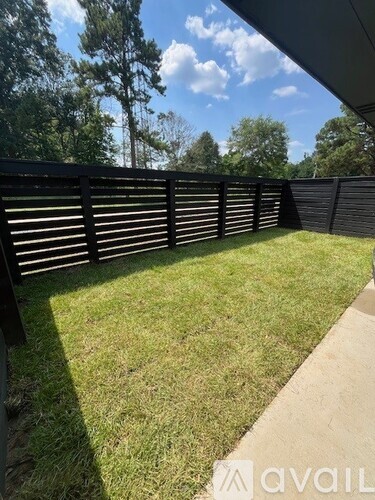 A black fence with slats separates a grassy area from a concrete path.
