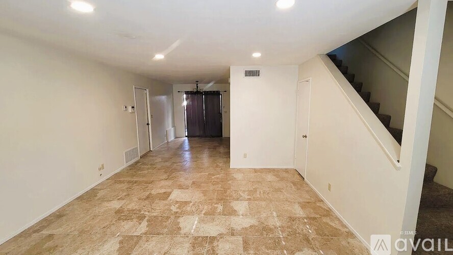 A spacious room with tiled flooring and a staircase on the right side.