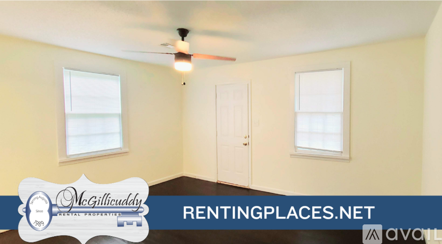 A room with a ceiling fan and two windows, with a sign for McGillicuddy Realty.