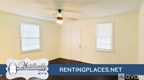 A room with a ceiling fan and two windows, with a sign for McGillicuddy Realty.
