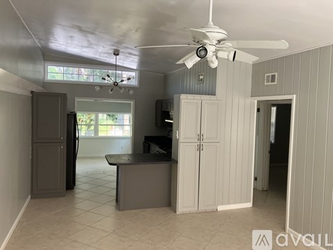 A room with a ceiling fan and a kitchen area with cabinets and a counter.