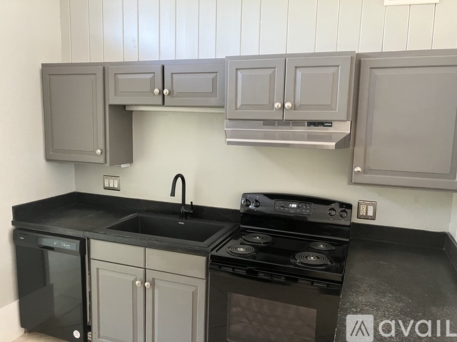 A kitchen with grey cabinets and a black countertop.