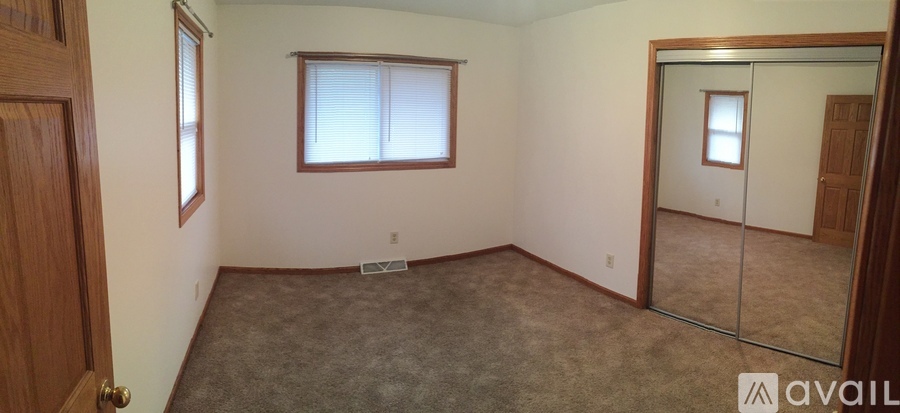 A room with a carpeted floor, a door, a window with blinds, and a mirror on the wall.