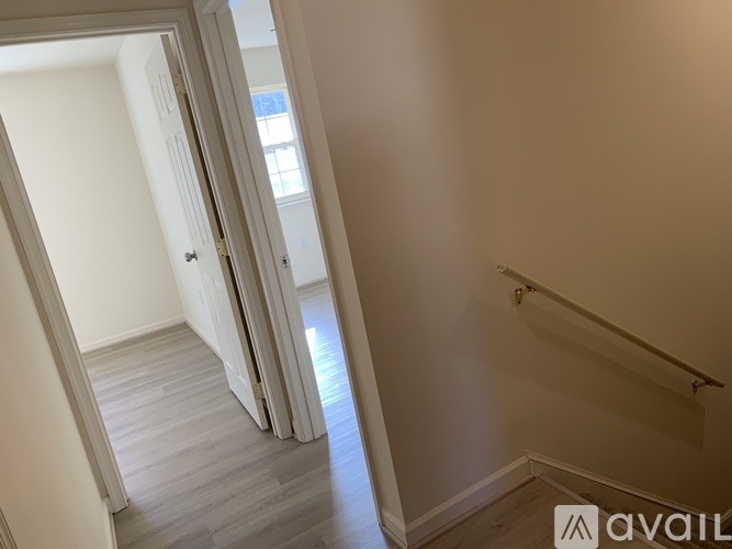 A hallway with a wooden floor and white walls leading to a door.