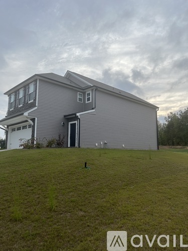 A grey house with a white door and windows is set on a grassy field.