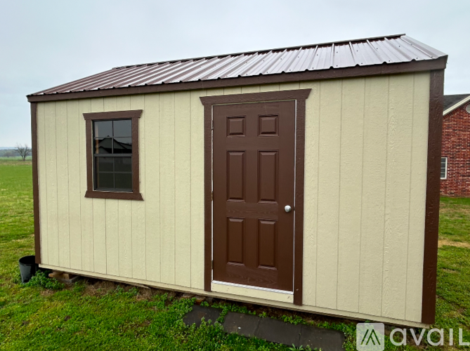 A small house with a brown door and window is on a grassy field.