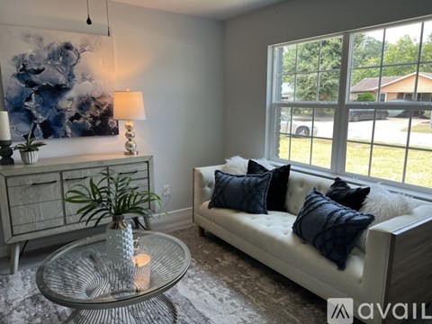 A living room with a white couch, a glass table, and a large painting on the wall.