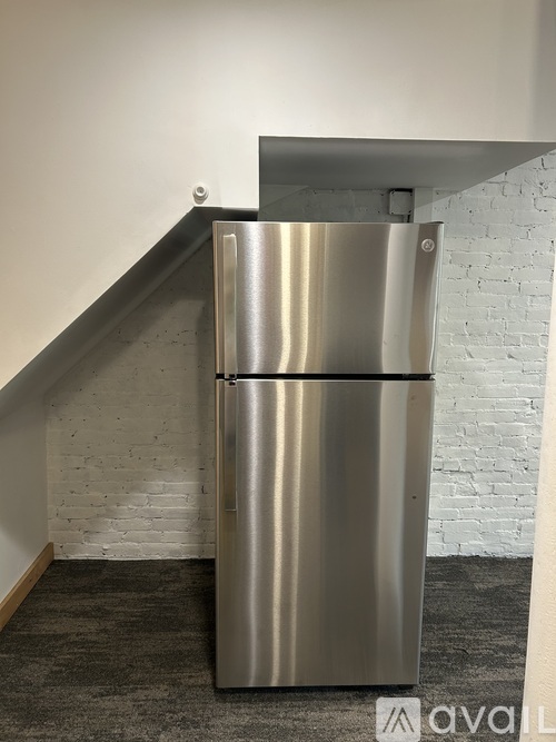 A stainless steel refrigerator in a room with a white brick wall.