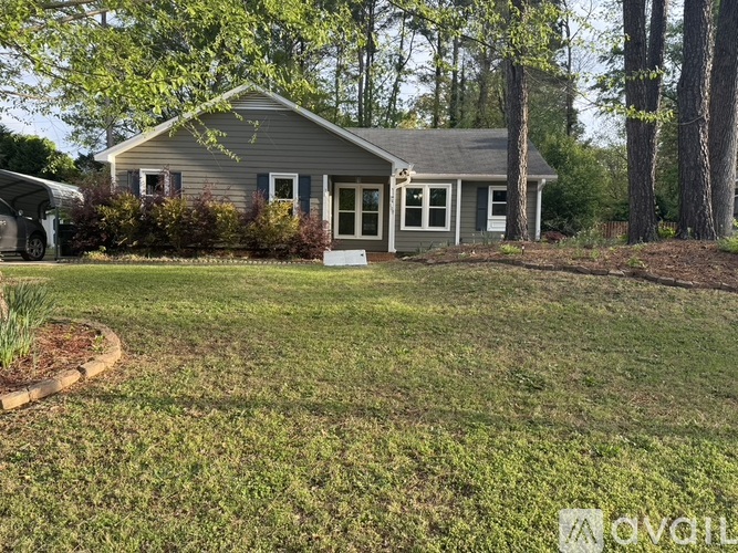 A house with a grey roof and white trim is surrounded by a grassy yard and trees.