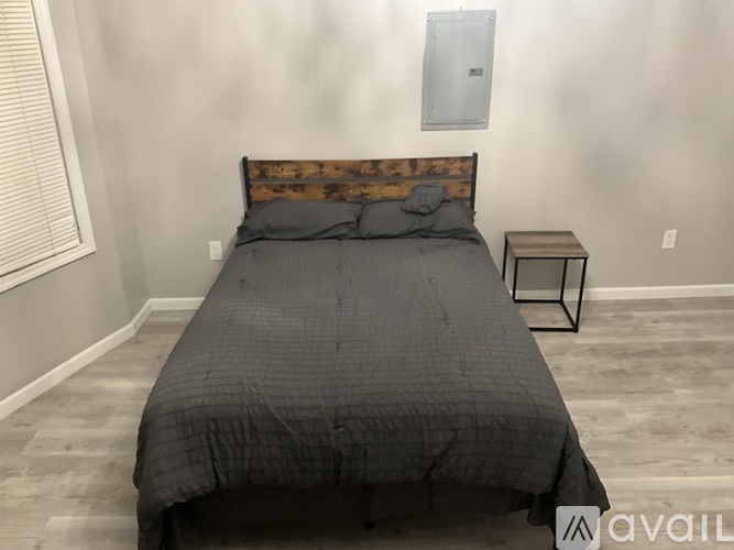 A bed with a wooden headboard and a grey comforter is in a room with a small table beside it.