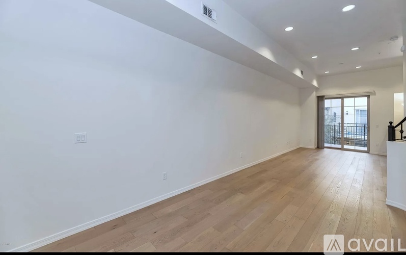 A spacious room with wooden flooring and a doorway leading to another room.