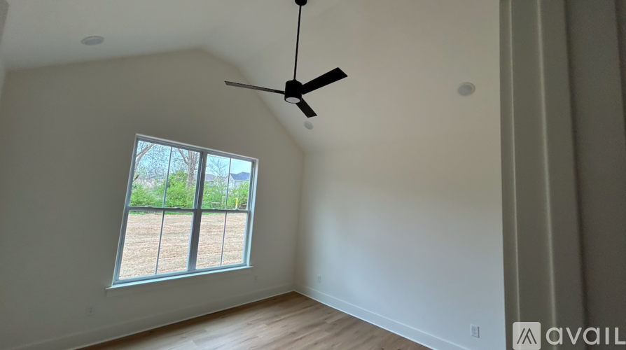 A room with a ceiling fan and a window overlooking a fenced area.