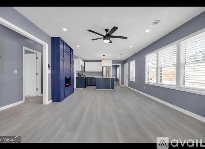 A spacious room with a ceiling fan and a kitchen area in the background.