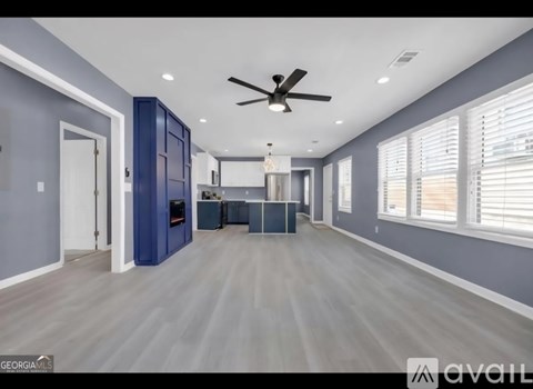 A spacious room with a ceiling fan and a kitchen area in the background.