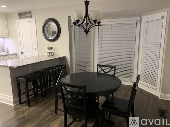 A black table with four chairs is in front of a kitchen island with a marble countertop.