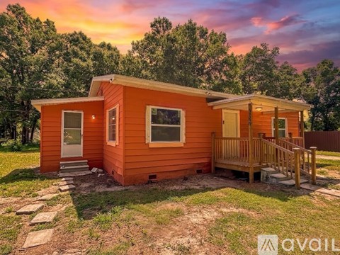 A small orange cabin with a porch and a stone pathway leading to the front door.