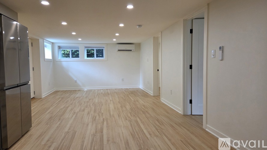 A spacious room with wooden flooring and a refrigerator on the left side.