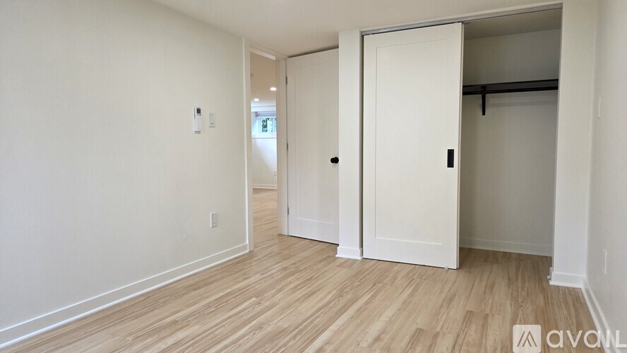 A room with white walls and wooden flooring, featuring a white door and a white closet.