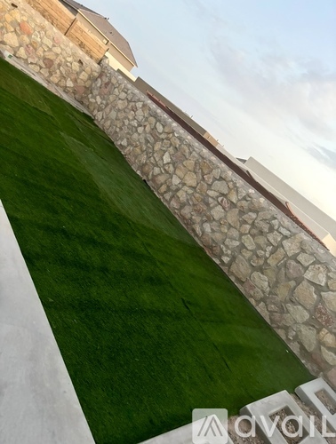 A stone wall separates a grassy area from a building.