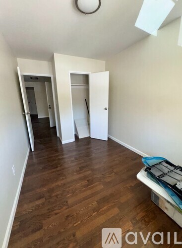 A room with wooden floors and white walls, with a bed and a suitcase on the floor.