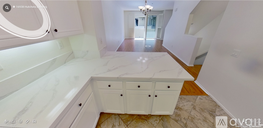 A white kitchen with a marble counter top and a chandelier hanging from the ceiling.
