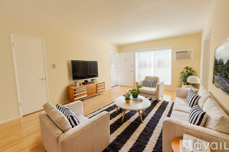 A living room with a white sofa, a white armchair, a coffee table, and a television on a wooden cabinet.