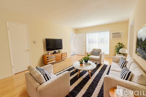 A living room with a white sofa, a white armchair, a coffee table, and a television on a wooden cabinet.
