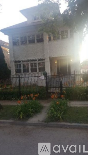 A white house with a black fence and flowers in front.