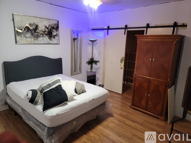 A bedroom with a bed, wooden wardrobe, and a painting on the wall.