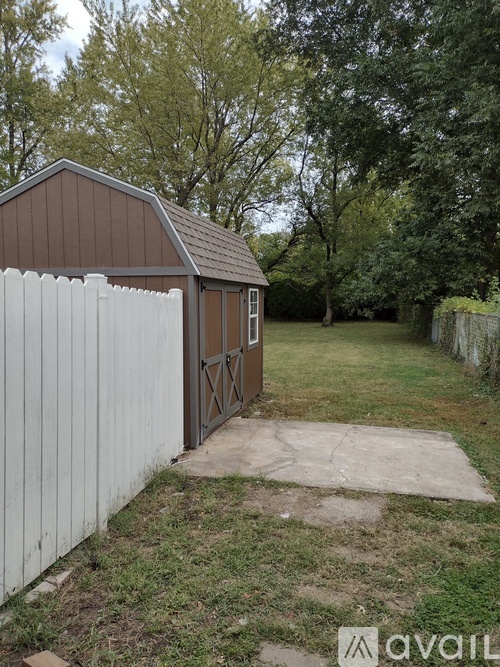 A shed with a brown roof and a white fence.